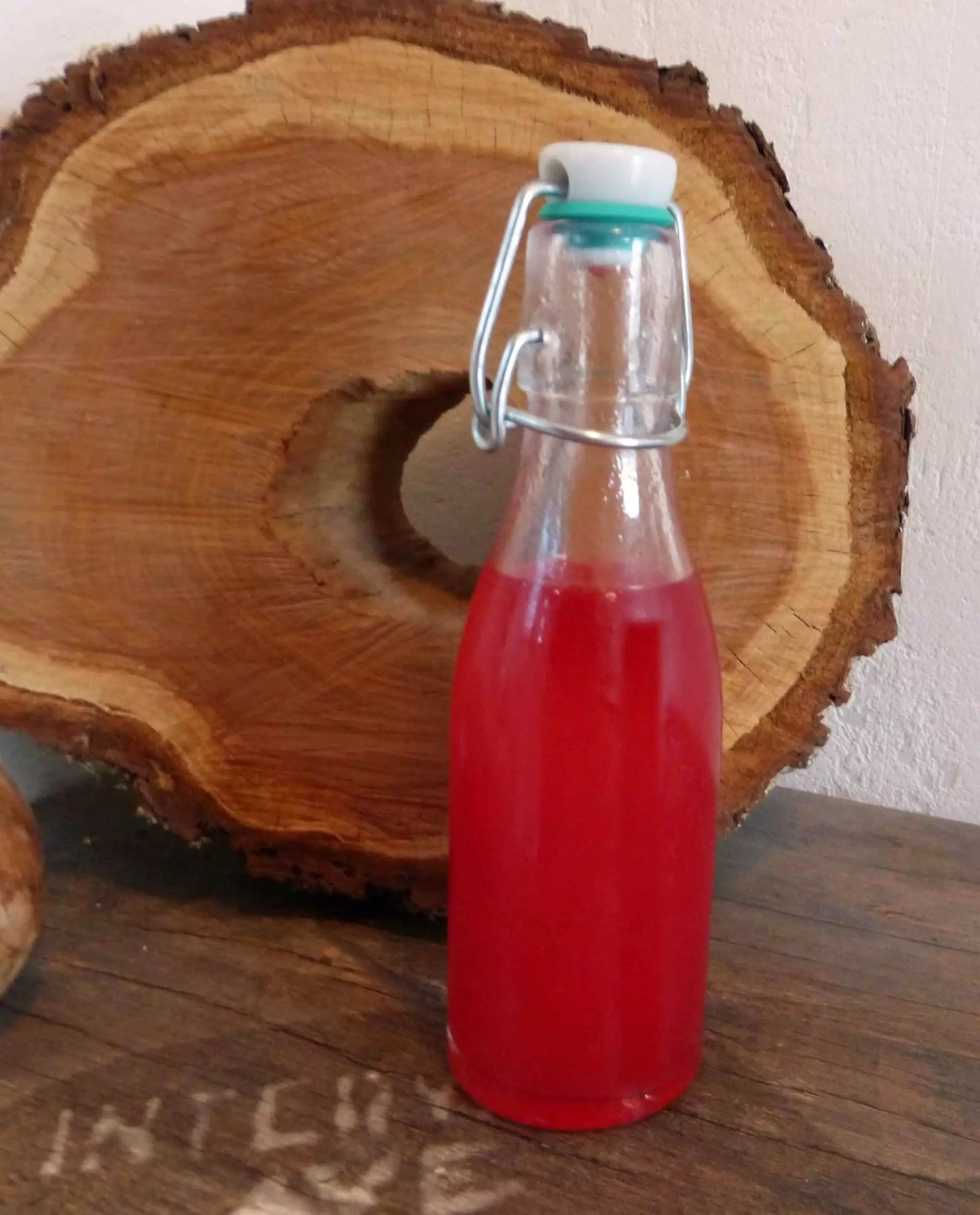 Eine Flasche Johannisbier-Sirup neben einem Stück Holz.