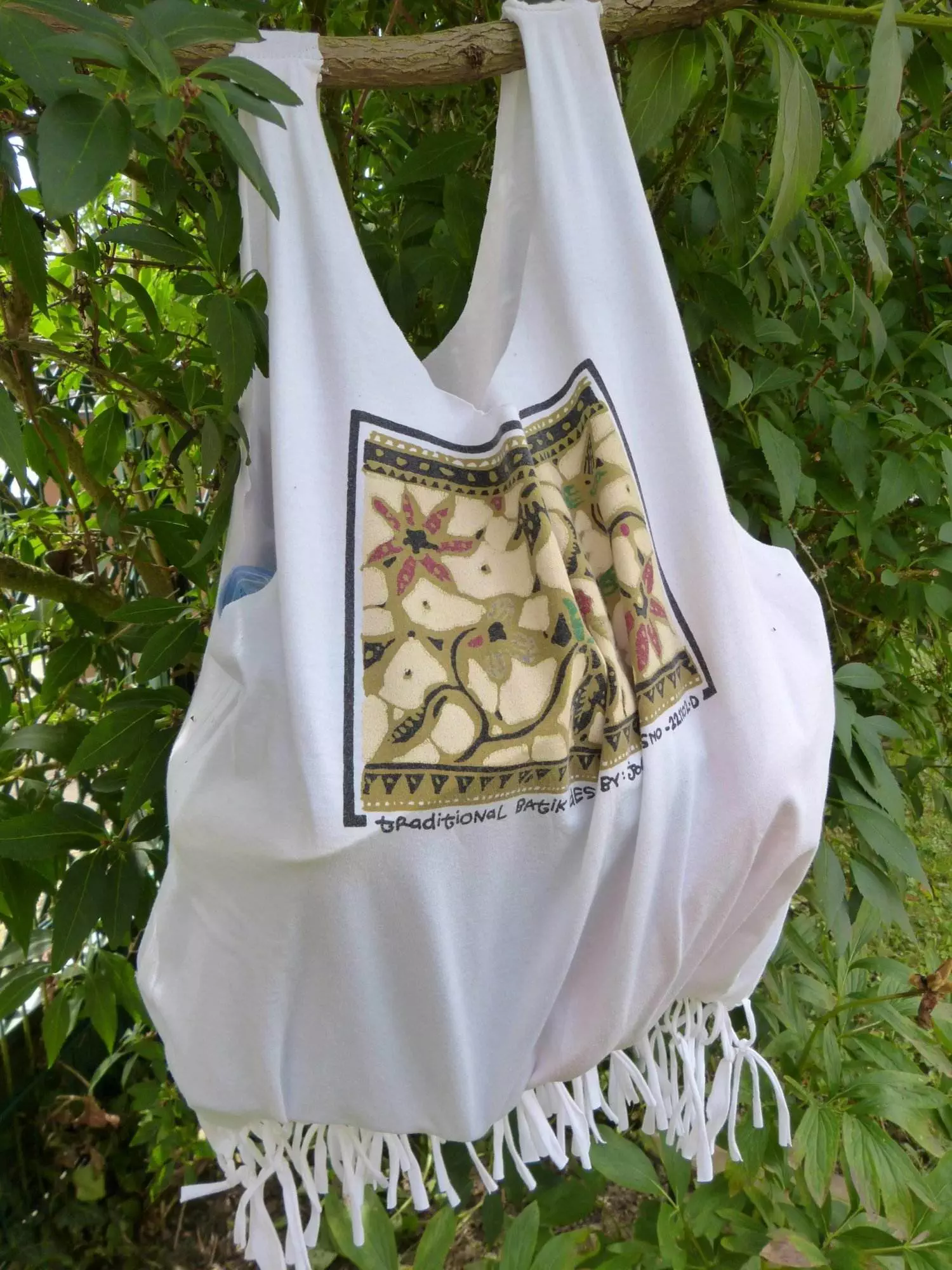 Eine weiße Einkaufstasche, die aus recyceltem T-Shirt-Material umfunktioniert wurde und an einem Baum hängt.