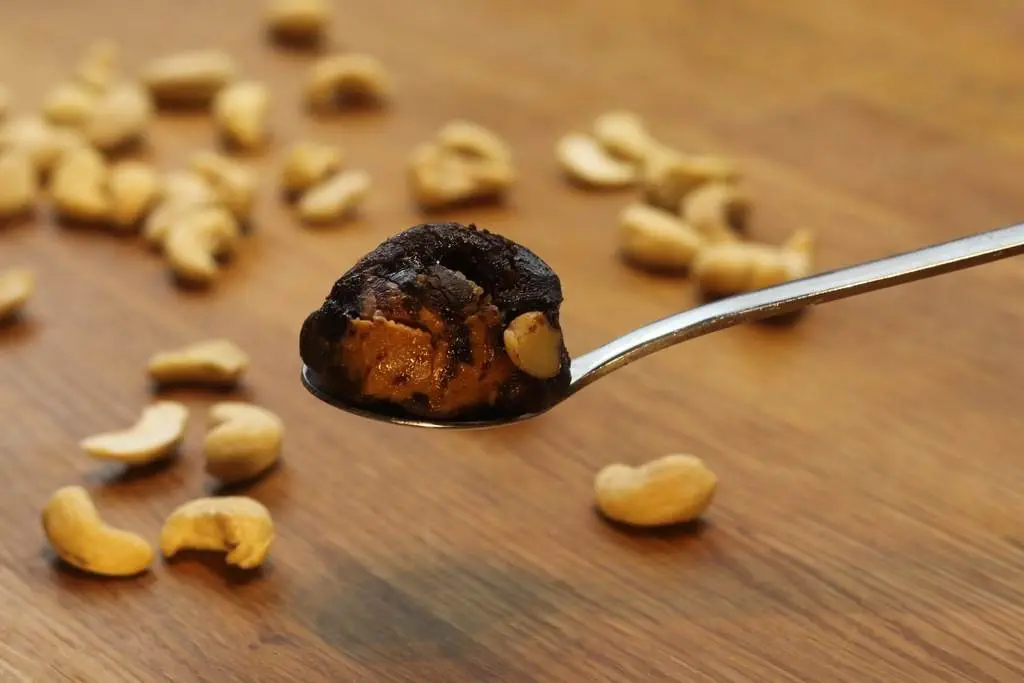 Ein Holztisch, geschmückt mit einem Löffel voller Cashewnüsse mit Schokoladenüberzug und veganen Brownies.