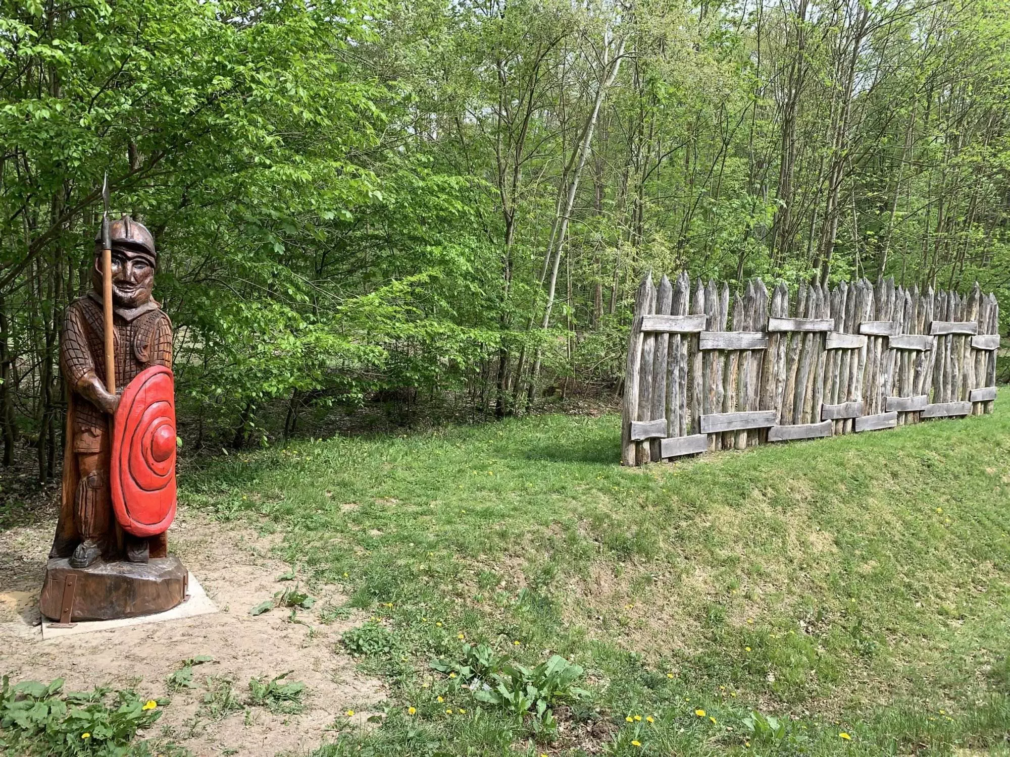 Eine hölzerne Statue eines Kriegers in einem Waldgebiet.