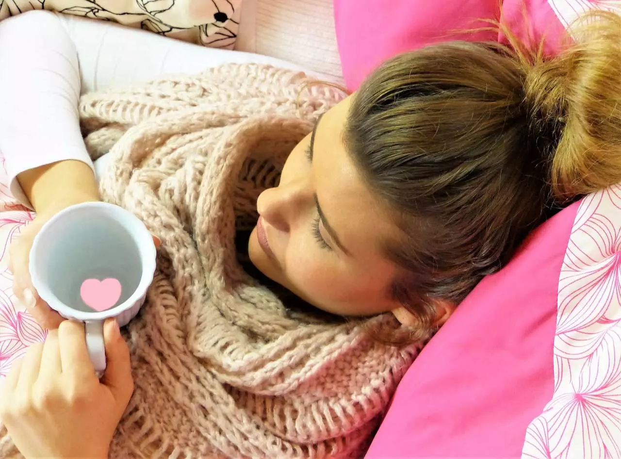 Eine Frau liegt mit einer Tasse Kaffee im Bett.